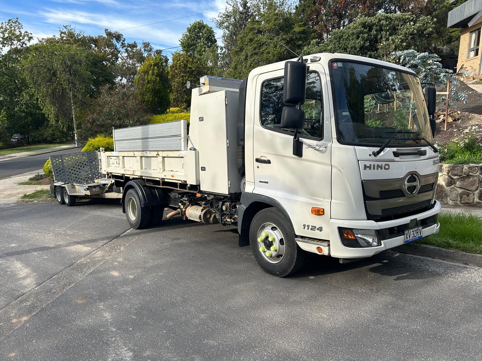 White Hino 1124 tipper truck towing a plant trailer on a residential street