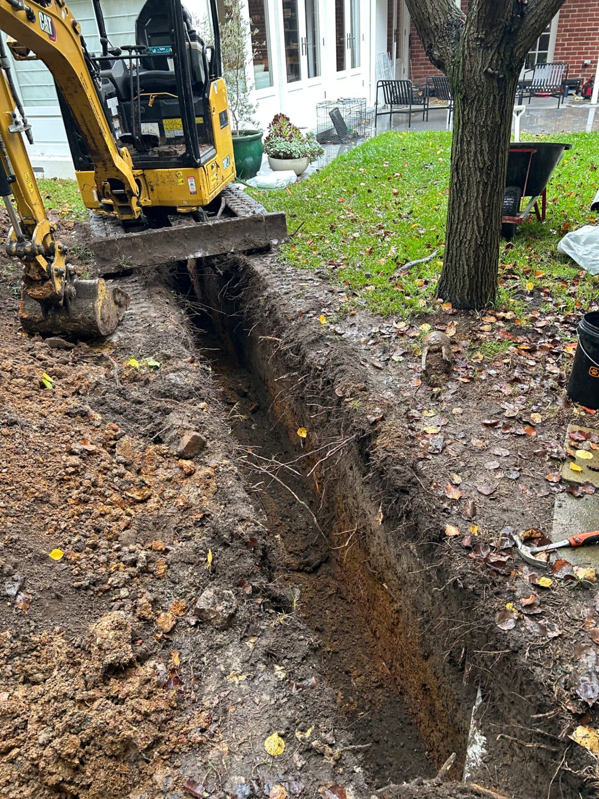 Narrow trench dug close to a tree and house wall in wet ground