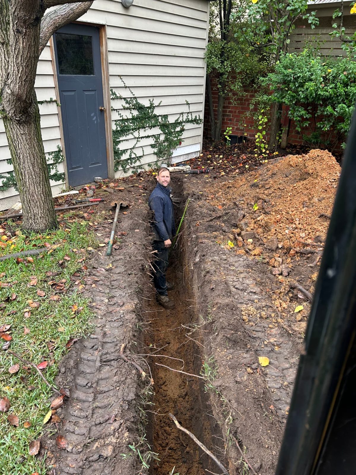 Worker standing chest-deep in a completed service trench, showing the depth achieved