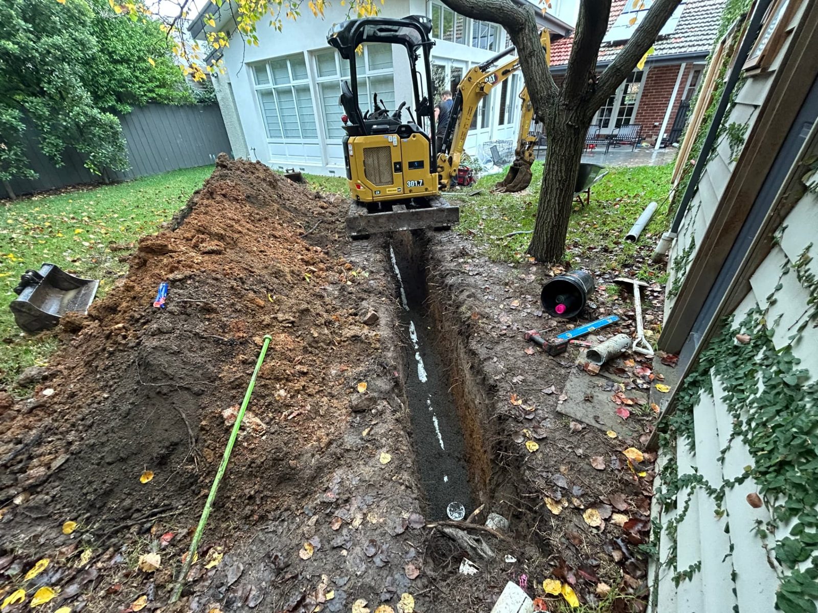 Deep service trench excavated along a lawn beside a period home with spoil stockpiled to one side