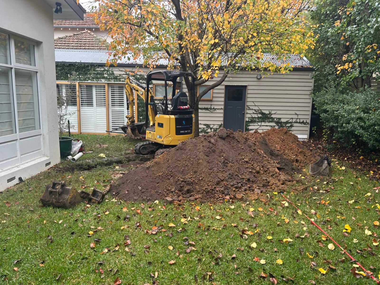 Spoil heaped beside the completed trench with buckets and attachments on the lawn