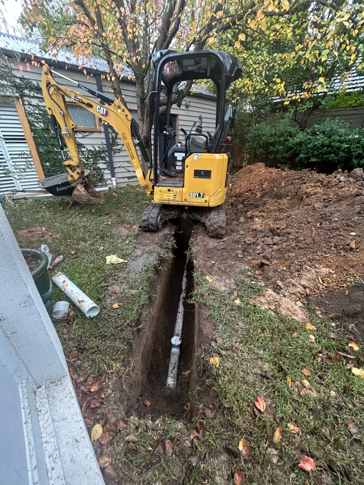Pipe laid in the base of a trench with the branded Rigid Earthworks excavator straddling the line